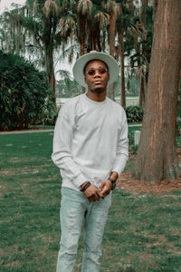 a man in a white hat and jeans standing in a park
