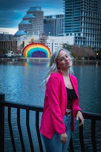 a woman in a pink jacket standing next to a lake